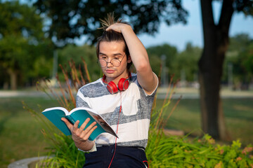 Young gay man reading a book in a park