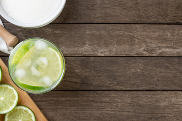 Brazilian lemon caipirinha in a glass with ice with fruit slices over wooden board  with copy space
