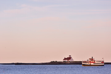 Obraz premium Beautiful Lighthouse Wood Island, Maine and Cruise boats at Sunset Viewing from Great Island Common state park, New Hampshire. 