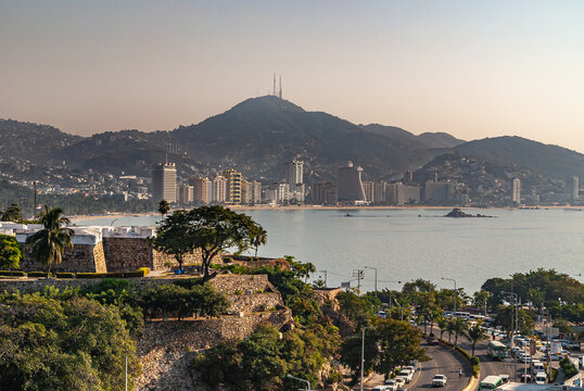 Acapulco, Mexico - November 25, 2008: Corner ramparts of Fort, Fuerte de San Diego, AKA Museo Historico, looks over bay with mountains and high rise buildings on horizon. Green foliage and freeway.