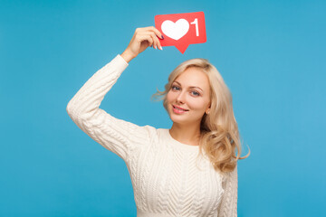 Woman with blond curly hair holding in hands like counter sign, rating posts in social networks, blogging. Indoor studio shot isolated on blue background