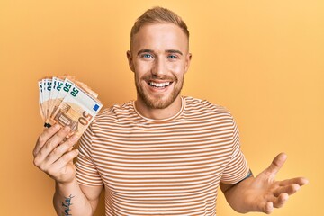 Young caucasian man holding bunch of 50 euro banknotes celebrating achievement with happy smile and...