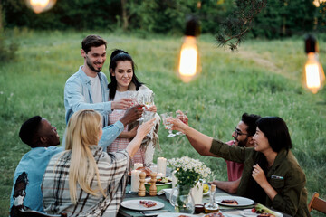 Three young cheerful intercultural couples toasting by served festive table