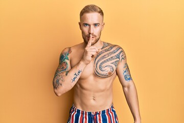 Fototapeta premium Young caucasian man wearing swimwear shirtless asking to be quiet with finger on lips. silence and secret concept.