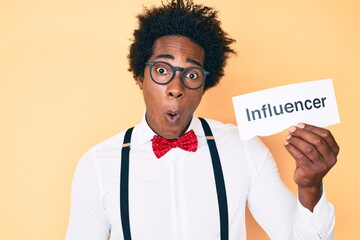 Handsome african american man with afro hair holding paper with influencer text scared and amazed with open mouth for surprise, disbelief face