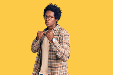 Handsome african american man with afro hair wearing casual clothes and glasses ready to fight with fist defense gesture, angry and upset face, afraid of problem