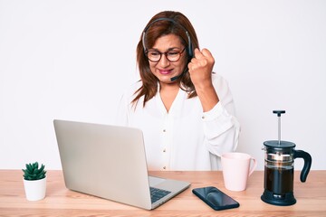 Middle age brunette hispanic woman working at the office wearing operator headset annoyed and frustrated shouting with anger, yelling crazy with anger and hand raised