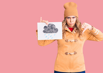 Young caucasian woman wearing winter clothes holding rain draw with angry face, negative sign...