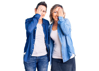 Couple of women wearing casual clothes covering one eye with hand, confident smile on face and surprise emotion.