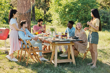 Young intercultural relaxed friends chatting by table after outdoor dinner
