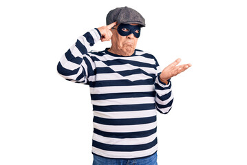 Senior handsome man wearing burglar mask and t-shirt confused and annoyed with open palm showing copy space and pointing finger to forehead. think about it.