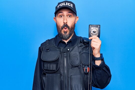Young handsome man wearing police uniform holding gun scared and amazed with open mouth for surprise, disbelief face