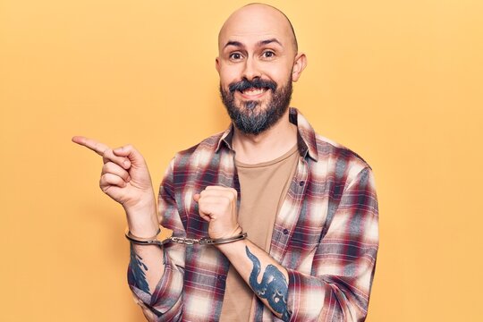 Young handsome man wearing prisoner handcuffs smiling happy pointing with hand and finger to the side