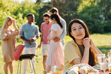 Young female of Asian ethnicity sitting by served table in front of camera