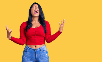 Hispanic woman with long hair wearing casual clothes crazy and mad shouting and yelling with aggressive expression and arms raised. frustration concept.
