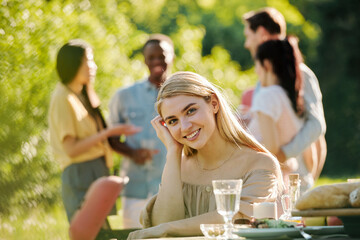 Young smiling woman with long blond hair looking at you while sitting by table