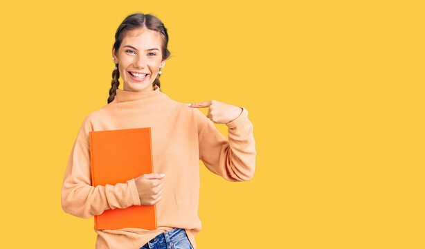 Beautiful caucasian woman with blonde hair holding book pointing finger to one self smiling happy and proud