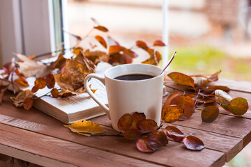 Autumn, autumn leaves, a hot steaming Cup of coffee and an old book on the background of a wooden table. Seasonal, morning coffee, Sunday relaxation and still life concept.