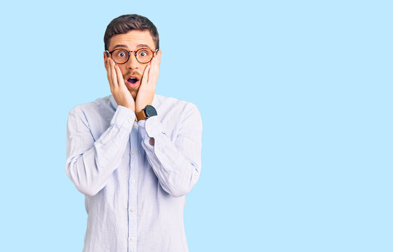 Handsome young man with bear wearing elegant business shirt and glasses afraid and shocked, surprise and amazed expression with hands on face