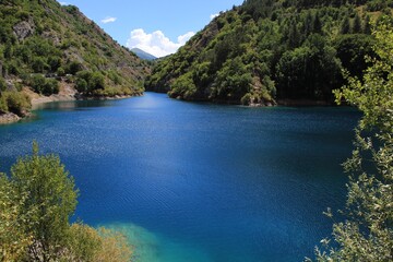 lake panorama, Abruzzi. Lush nature overlooking the surface of Lake San Domenico. Green hills plunge into the emerald waters. Green trees, summer sky of a sunny July day. Glimpse of bright colors