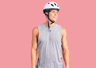 Young handsome man wearing bike helmet looking away to side with smile on face, natural expression. laughing confident.