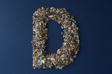 The letter D is lined with small pebbles on a blue background