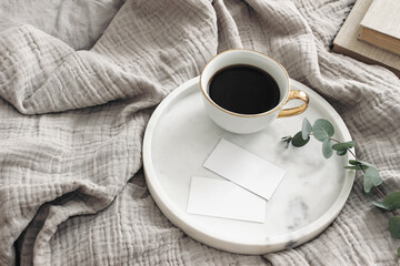 Breakfast in bed stationery mockup scene. Cup of coffee, blank business cards on white marble tray. Green eucalyptus tree branch and books on muslin throw. Lifestyle concept. High angle view. - obrazy, fototapety, plakaty