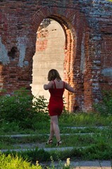 Fototapeta na wymiar pretty girl in short red dress on background of green forest and brick walls