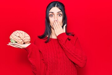 Young beautiful girl holding brain covering mouth with hand, shocked and afraid for mistake....