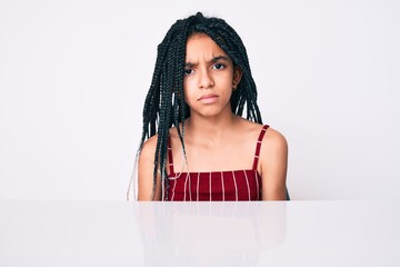 Young african american girl child with braids wearing casual clothes sitting on the table skeptic and nervous, frowning upset because of problem. negative person.