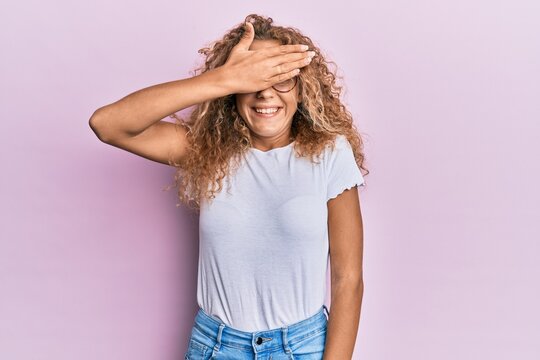 Beautiful caucasian teenager girl wearing white t-shirt over pink background smiling and laughing with hand on face covering eyes for surprise. blind concept.