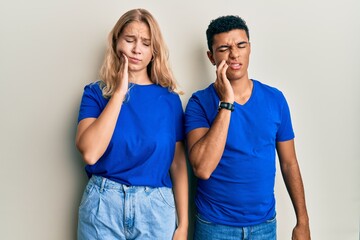 Fototapeta premium Young interracial couple wearing casual clothes touching mouth with hand with painful expression because of toothache or dental illness on teeth. dentist