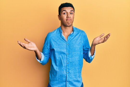 Young arab man wearing casual clothes clueless and confused expression with arms and hands raised. doubt concept.