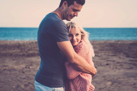 Love and protection couple with a young beautiful couple in relationship hugging and loving each other - girl and boy enjoying the outdor leisure activity at the beach in autumn season