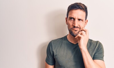 Young handsome man wearing casual t-shirt standing over isolated white background thinking concentrated about doubt with finger on chin and looking up wondering