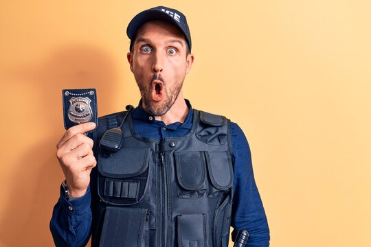 Young handsome policeman wearing uniform and bulletprof holding police badge scared and amazed with open mouth for surprise, disbelief face