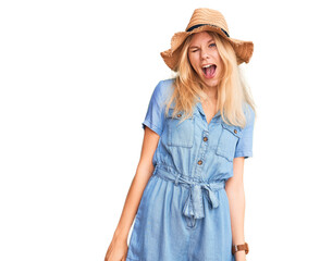 Young beautiful blonde woman wearing summer hat and dress winking looking at the camera with sexy...
