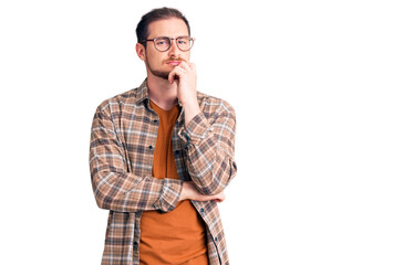 Young handsome caucasian man wearing casual clothes and glasses serious face thinking about question with hand on chin, thoughtful about confusing idea