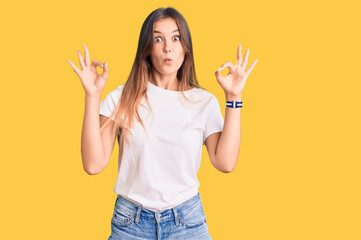 Beautiful caucasian woman wearing casual white tshirt looking surprised and shocked doing ok approval symbol with fingers. crazy expression