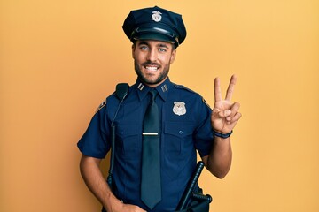 Obraz premium Handsome hispanic man wearing police uniform showing and pointing up with fingers number two while smiling confident and happy.