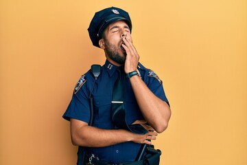 Handsome hispanic man wearing police uniform bored yawning tired covering mouth with hand. restless...