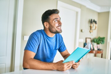 Young handsome man smiling happy reading book at home