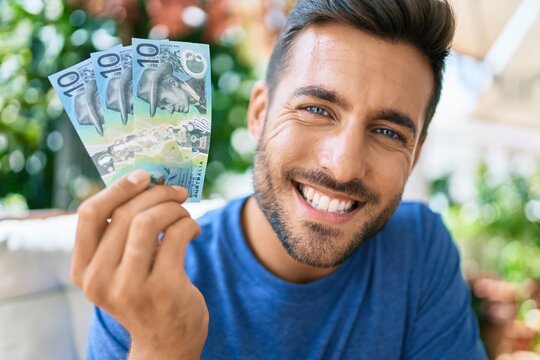 Young hispanic man smiling happy holding australian dollars banknotes at the terrace.