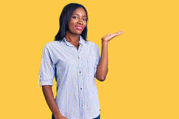 Young african american woman wearing casual clothes smiling cheerful presenting and pointing with palm of hand looking at the camera.