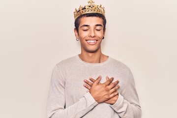 Young african amercian man wearing prince crown smiling with hands on chest with closed eyes and grateful gesture on face. health concept.