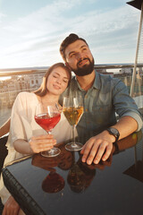 Vertical shot of two young people in love cuddling on sunset, drinking wine at bar terrace
