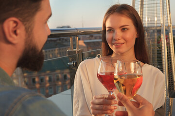 Beautiful woman smiling at her man, clinking wine glasses, celebrating anniversary on bar terrace on sunset