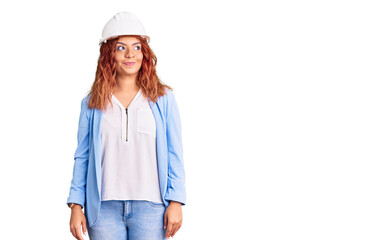 Young latin woman wearing architect hardhat smiling looking to the side and staring away thinking.