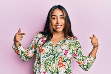 Young latin woman wearing casual clothes looking confident with smile on face, pointing oneself...
