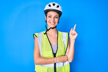 Young caucasian girl wearing bike helmet and reflective vest smiling happy pointing with hand and finger to the side